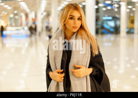 Beautiful young woman in a trendy gray coat with a stylish scarf in the mall