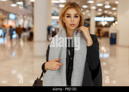 Beautiful stylish young blond woman in a trendy gray scarf and coat at the mall