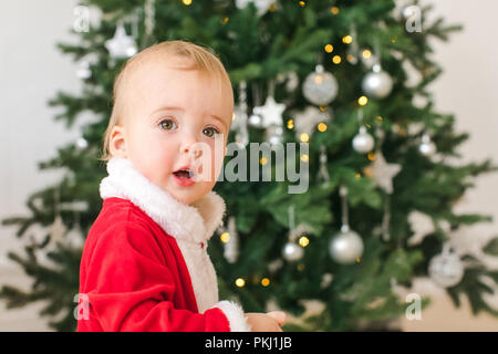 Little boy in Santa costume standing near Christmas tree Stock Photo