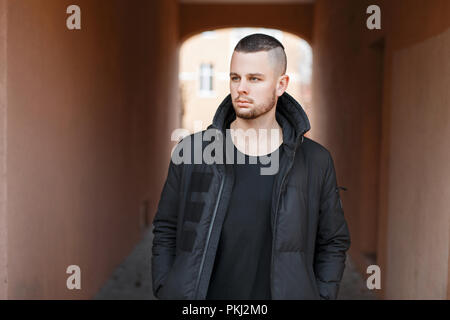 Handsome fashionable man in black stylish winter jacket walking on the street Stock Photo