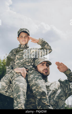 low angle view of family in military uniform saluting with cloudy sky on backdrop Stock Photo