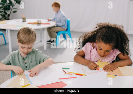 multicultural preschoolers drawing pictures with pencils in classroom Stock Photo