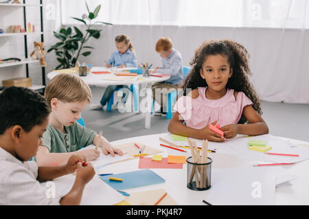 multicultural preschoolers drawing pictures with pencils in classroom Stock Photo