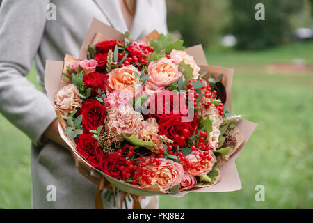 lovely woman holding a beautiful autumn bouquet flower arrangement with carnations and red garden roses color pink green lawn on background pkj8b2
