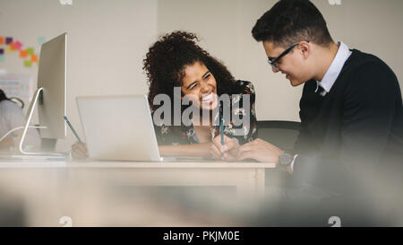 Businessman and woman sharing moments of laughter during work. Happy business colleagues discussing ideas sitting at the desk with laptop computer. Stock Photo