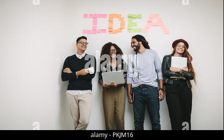 Cheerful business colleagues standing in office against a wall with the word idea written with sticky notes. business colleagues in cheerful mood rela Stock Photo