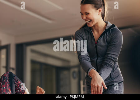 Female trainer guiding woman during pilates training at a gym. Female pilates instructor laughing while training woman in a gym. Stock Photo