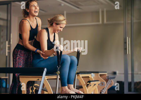 Smiling woman at the gym doing pilates training with her trainer. Trainer helping woman in pulling the stretch bands while doing pilates workout. Stock Photo