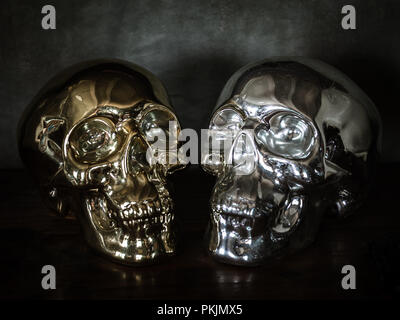 Old golden and silver human skull face on old wooden table and cement grunge wall background. Stock Photo