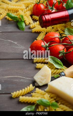Italian food - raw fusilli, tomato, basil and wine on the wooden table. Stock Photo