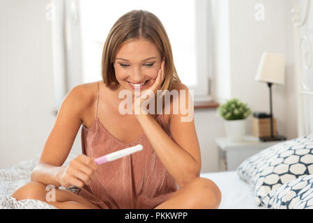 Young happy woman because of the pregnancy test result. Woman holding a pregnancy test in hands Stock Photo