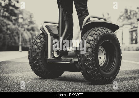 Close up detail of the wheels of a Segway personal transporter with the legs of a person in pants, greyscale image on asphalt Stock Photo