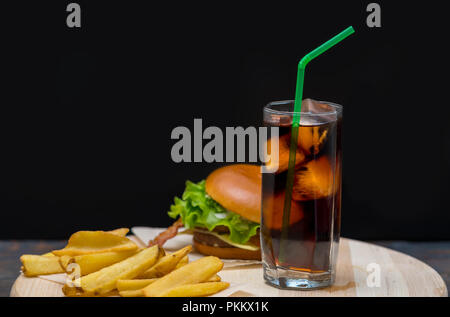 Hamburger served with French fries and a tall glass of chilled soda or coke with a straw over a dark background with copy space Stock Photo