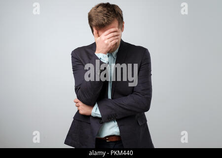 Feeling depressed concept. Exhausted young man in suit covering face with hand Stock Photo