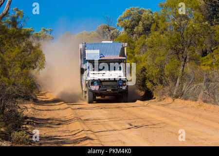 Land Rover campervan throwing up clouds of dust on red Australia outback road hemmed with bushland under blue sky in Queensland Stock Photo