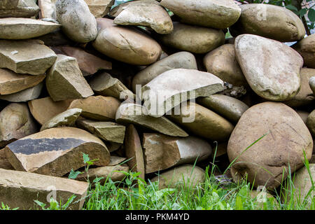 Lit by sun pile of big crackled different sizes and shapes light soft brown stones on green grass. Natural resources, building material, construction  Stock Photo