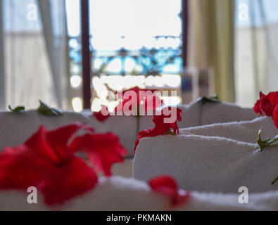 hibiscus petals on bed with beautiful sea view in background, White towels decoration surrounded by hibiscus petals Stock Photo