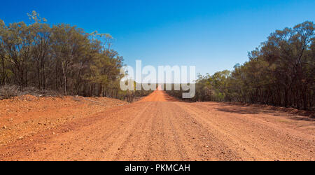 Long red Australian outback road slicing through landscape cloaked with bushland & stretching to horizon under blue sky Stock Photo