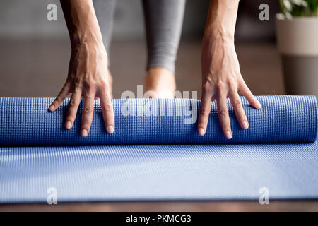 Girls hand folding blue exercise mat on the floor Stock Photo