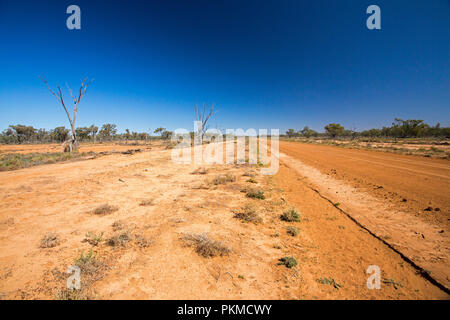 Red Australian outback road slicing through arid landscape with sparse  vegetation during drought & stretching to distant horizon under blue sky Stock Photo