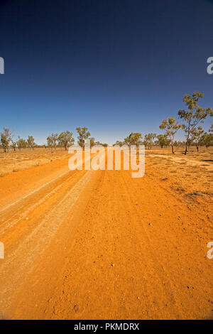 Red Australian outback road slicing through arid landscape with sparse  vegetation during drought & stretching to distant horizon under blue sky Stock Photo