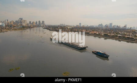 Aerial view tugboat pushes barge in the Bay of Manila. Tugboat and ship inside the harbor. Barge loaded with floats in the sea. Philippines, Manila. Stock Photo