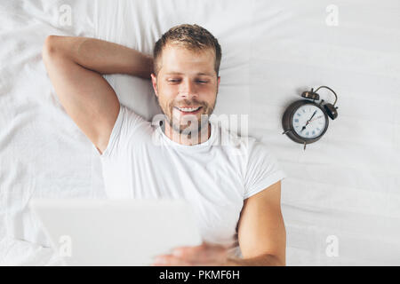 Handsome man using a digital tablet in bed at home Stock Photo