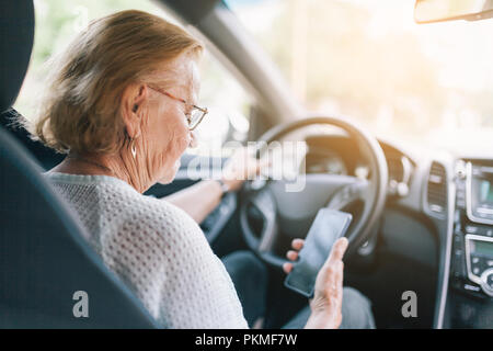 Elderly woman behind the steering wheel of a car using her phone Stock Photo