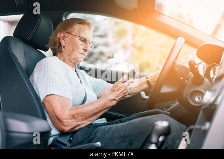 Elderly woman behind the steering wheel of a car using her phone Stock Photo