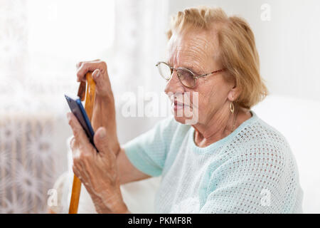 Elderly woman with glasses and cane using a mobile phone Stock Photo