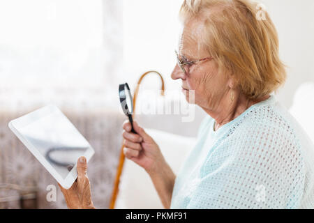 Elderly woman with glasses and loupe using a modern digital tablet Stock Photo