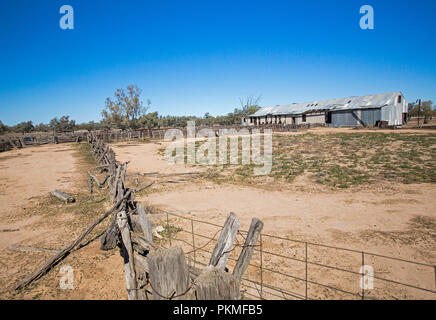 Old sheep shearing shed, fences and barren ground under blue sky in outback Australia during drought Stock Photo