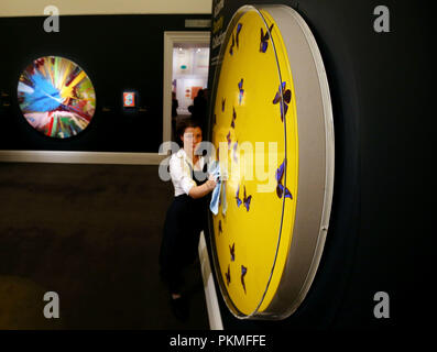 A gallery technician takes a dust cloth to the surface of Damien Hirst's 'Smashing Yellow Ball at Peace', at Sotheby's, New Bond Street, London, part of their forthcoming Yellow Ball: The Frank and Lorna Dunphy Collection sale, a collection from the former business manager of the artist. Stock Photo