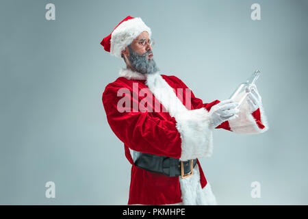 Funny guy with christmas hat posing at studio. New Year Holiday. Christmas, x-mas, winter, gifts concept. Man wearing Santa Claus costume on gray. Copy space. Winter sales. Stock Photo