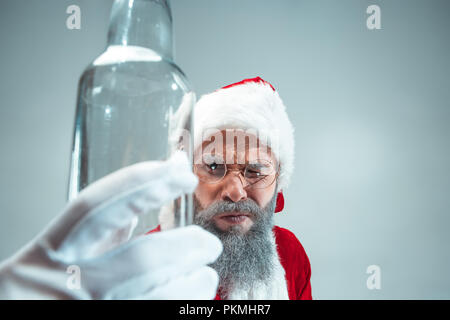 Funny guy with christmas hat posing at studio. New Year Holiday. Christmas, x-mas, winter, gifts concept. Man wearing Santa Claus costume on gray. Copy space. Winter sales. Stock Photo