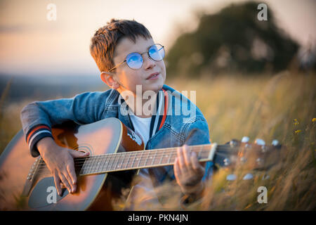 A little boy with glasses playing guitar in the field. Nature, beauty. Stock Photo