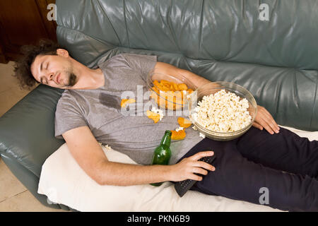 A man sleeping on a couch in a mess of junk food Stock Photo