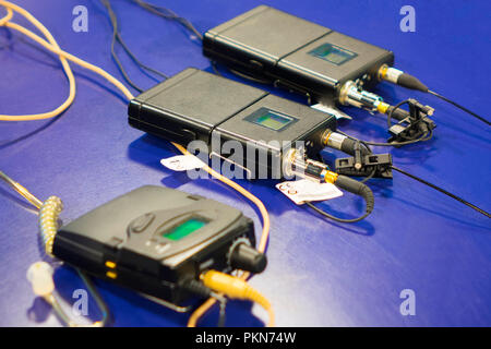 Three wireless microphone transmitter and three wireless microphone reciever on blue table in tv studio Stock Photo