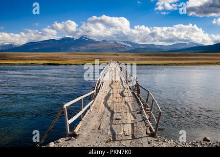 Shabby wooden bridge over a river with distant mountain range in background, Altai Mountains, Western Mongolia Stock Photo