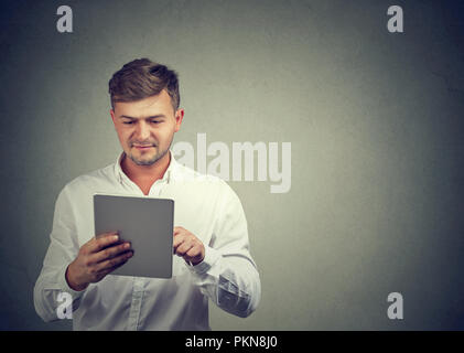 Content casual guy in white shirt browsing modern tablet enjoying new device standing on gray. Stock Photo
