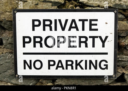 Private Property No Parking sign with black text on white background on an old stone wall. Stock Photo