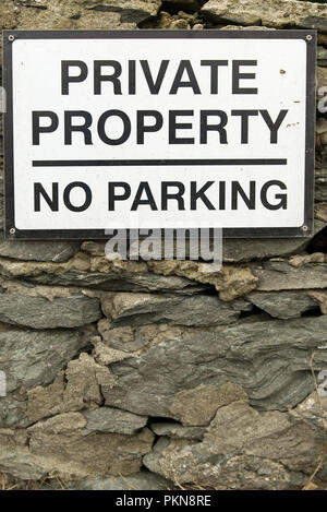 Private Property No Parking sign with black text on white background on an old stone wall. Stock Photo