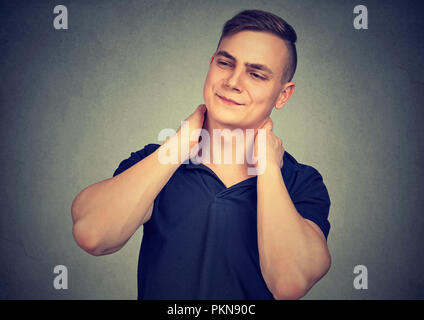Young man looking tired and rubbing neck having pain and looking away in frown on gray background Stock Photo