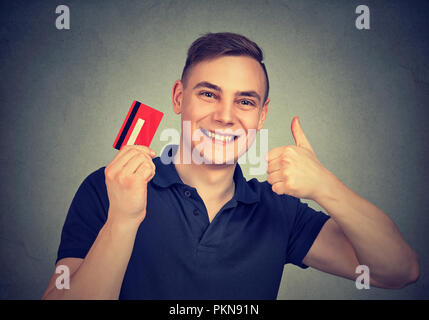 Young smiling man holding credit card and showing thumb up giving great rate Stock Photo