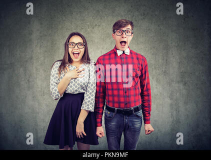 Young modern man and woman in eyeglasses screaming with astonishment and looking at camera on gray background Stock Photo