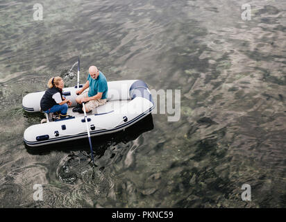 Looking down from above onto a senior couple rowing a dinghy across a calm ocean, river or lake with copy space Stock Photo