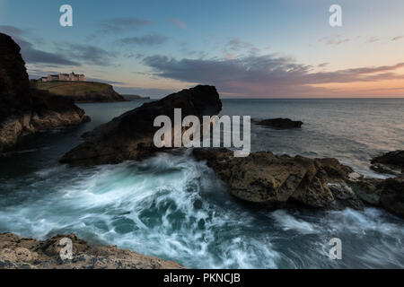 A rugged coastal sunset image of crashing waves flowing over harsh rocks using motion blur on the Cornish coast in Cornwall, UK. Stock Photo