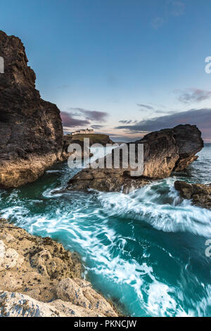 A rugged coastal sunset image of crashing waves flowing over harsh rocks using motion blur on the Cornish coast in Cornwall, UK. Stock Photo