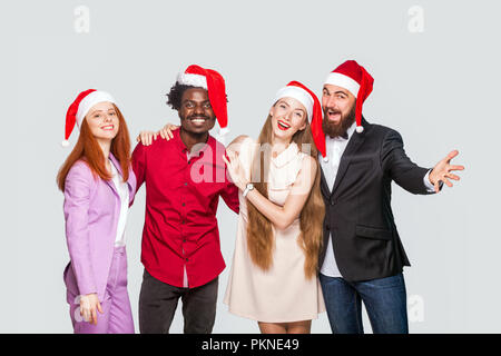 Group of beautiful happy handsome friends in red cap standing and celebrating new year, looking at camera with toothy smile. indoor studio shot, isola Stock Photo