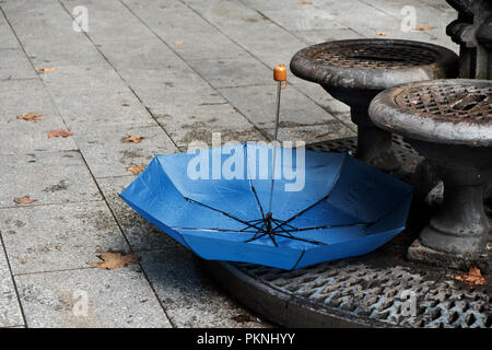 closeup of an umbrella upside down and some dry leaves on the pavement of a street in Barcelona, Spain, next to a public fountain Stock Photo